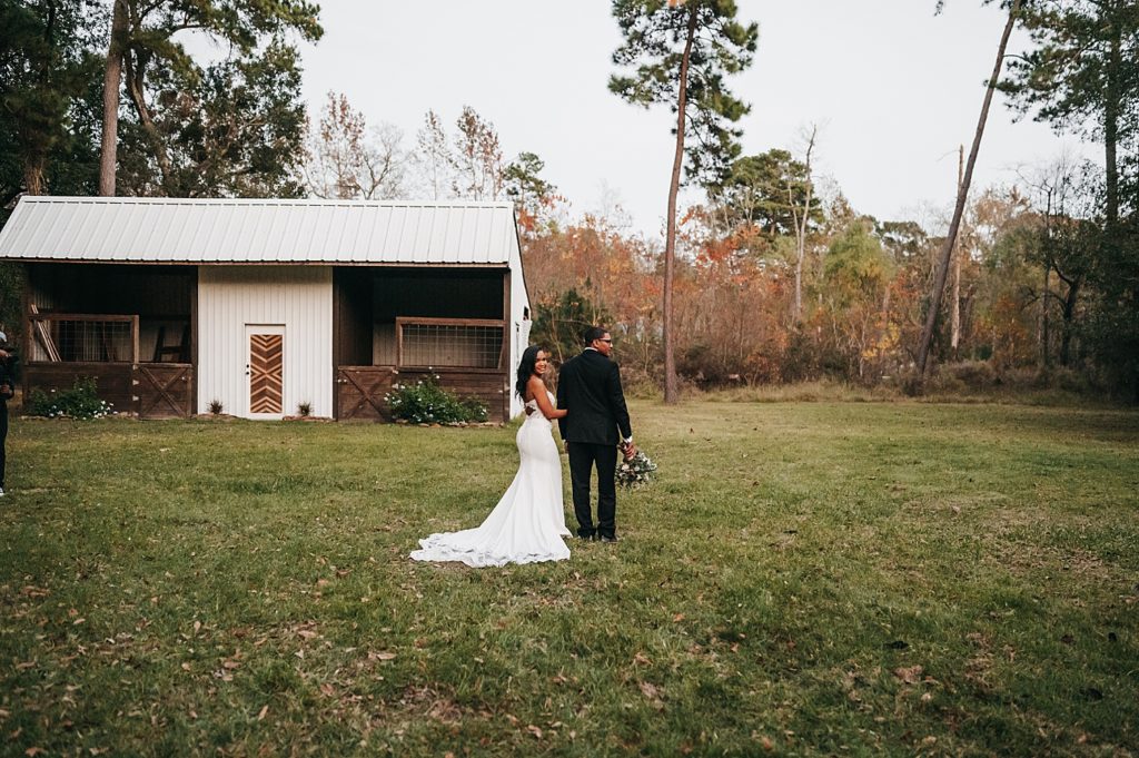 Bride and groom standing in a field in front of an hold house for their wedding portraits.