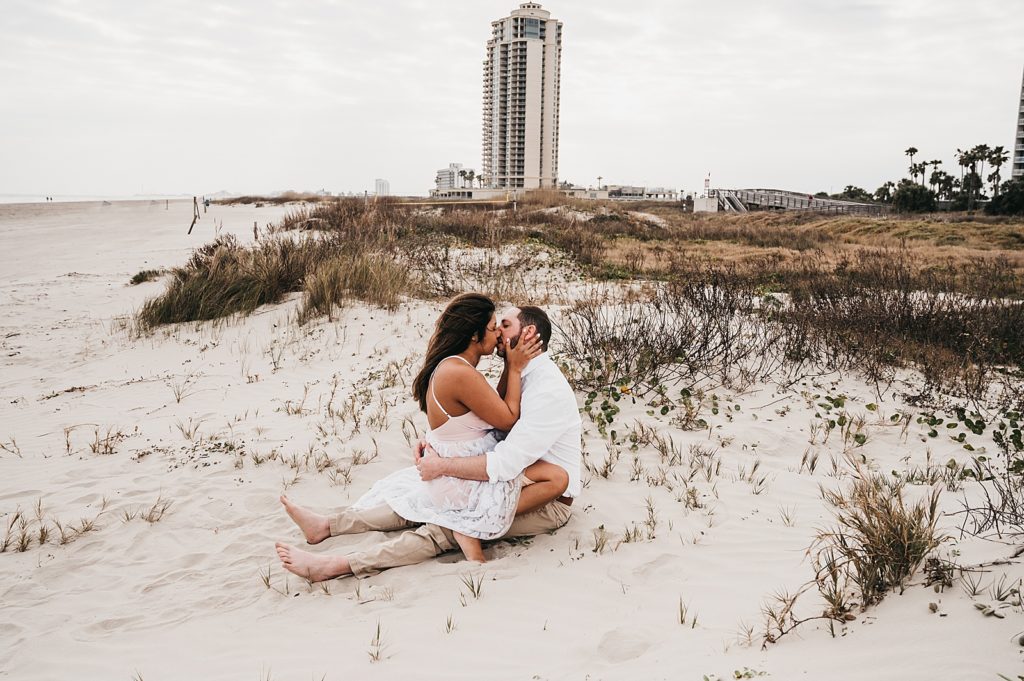 Woman sitting on man's lap and kissing him for beach photo shoot. 