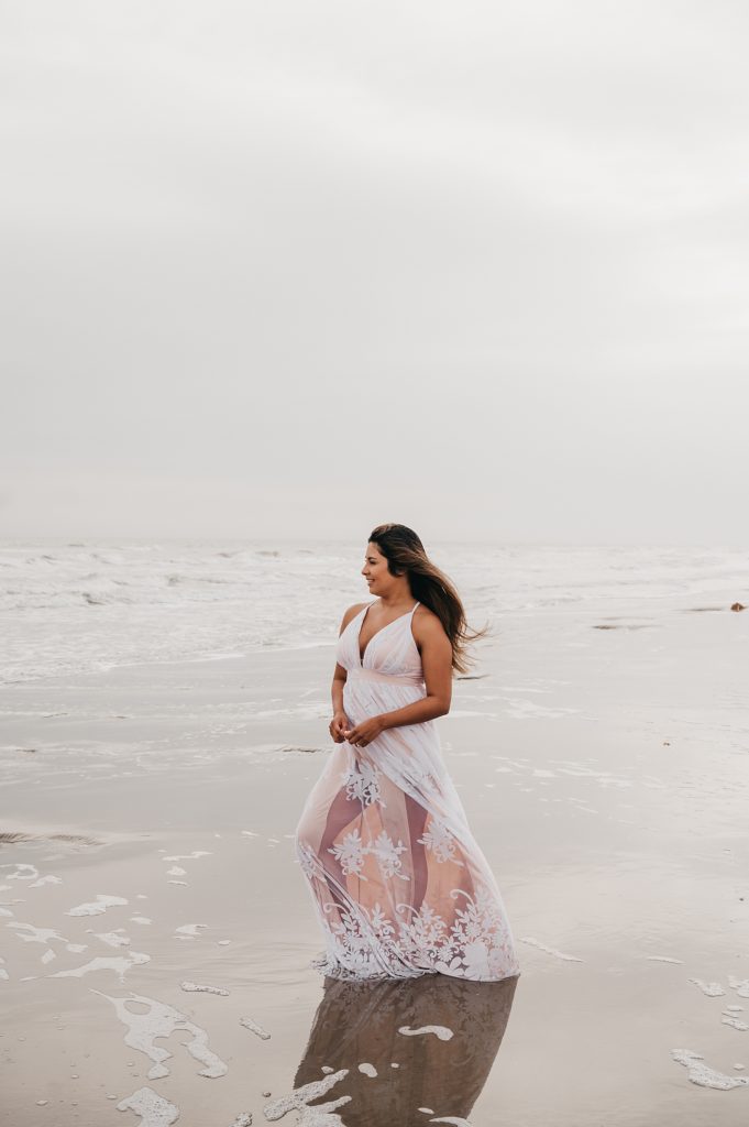 Woman in long lace dress standing in the water at the beach in Galveston, Texas. 