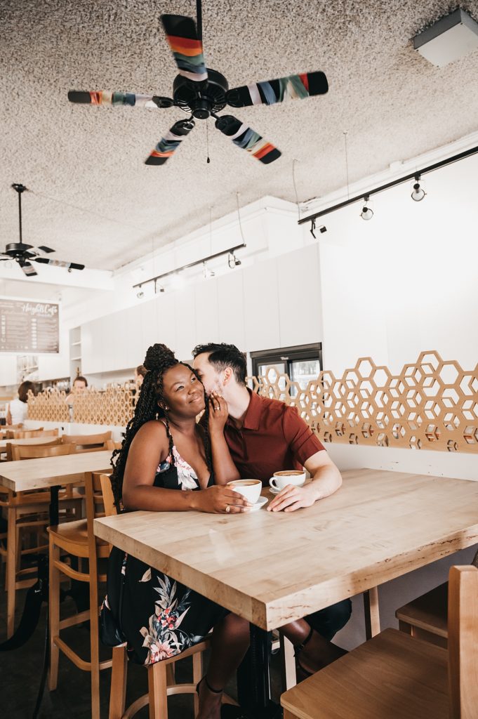 Man kissing woman's cheek during their Houston Heights coffee date engagement photos. 