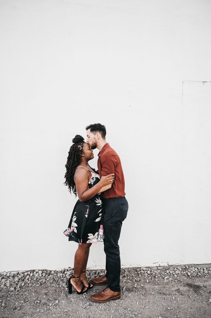 Man kissing woman's forehead in front of a white wall by Houston engagement photographer, Brittany Emanuel. 