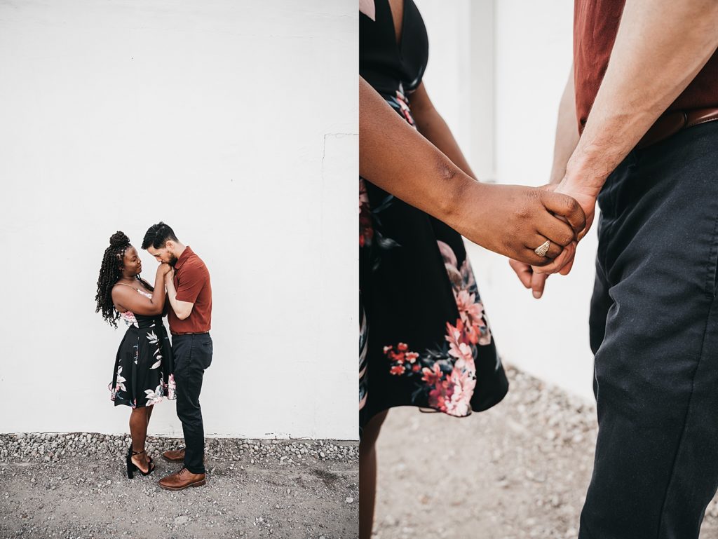 Engaged couple holding hands in front of a white wall for their photo shoot.