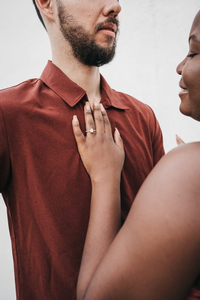 Woman's left hand with a diamond ring placed on a man's chest during their engagement photos. 
