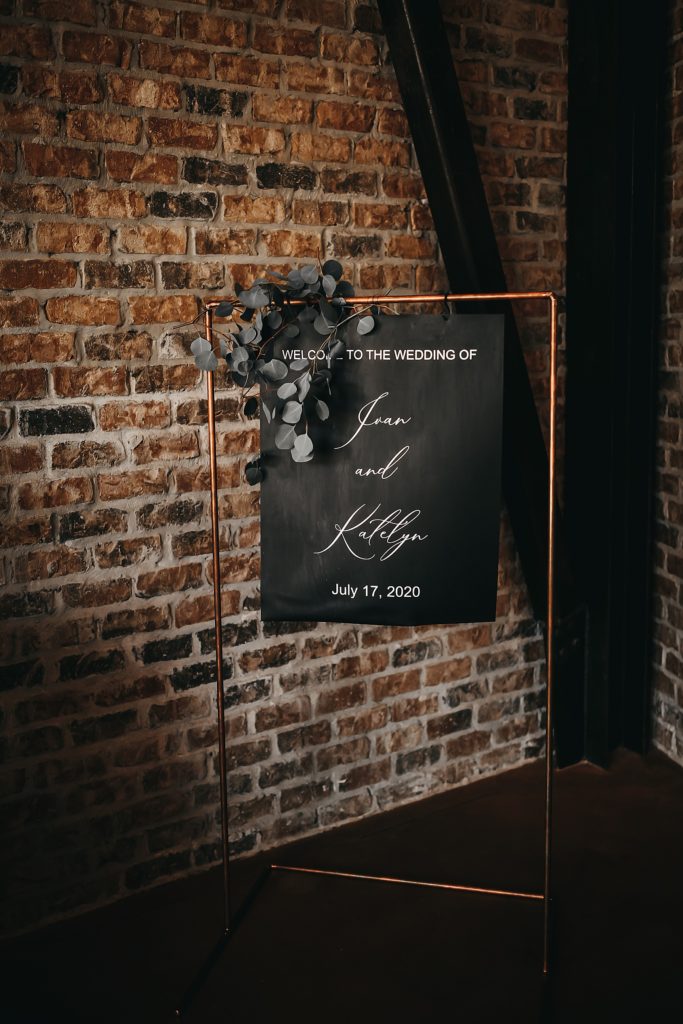 Black scripted wedding sign hung up in front of a exposed bring wall at this Texas wedding. 