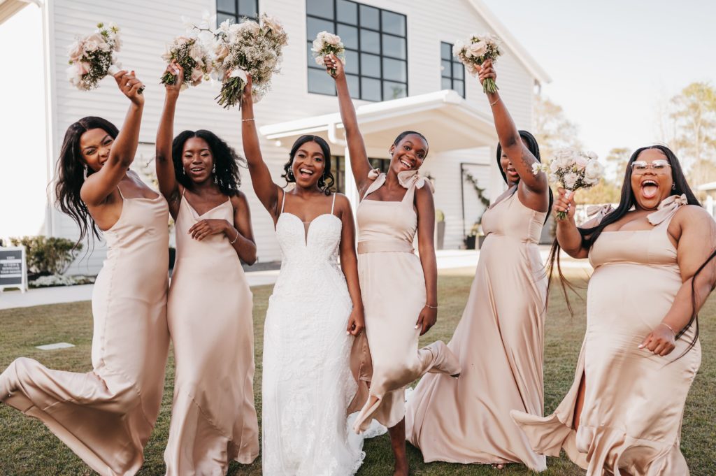 Bride and 5 bridesmaids smile while holding their bouquets in the air