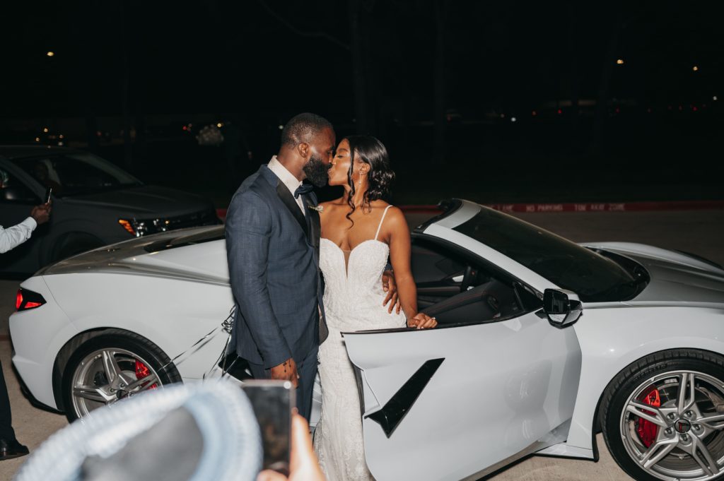 Bride and groom kiss by the white getaway car