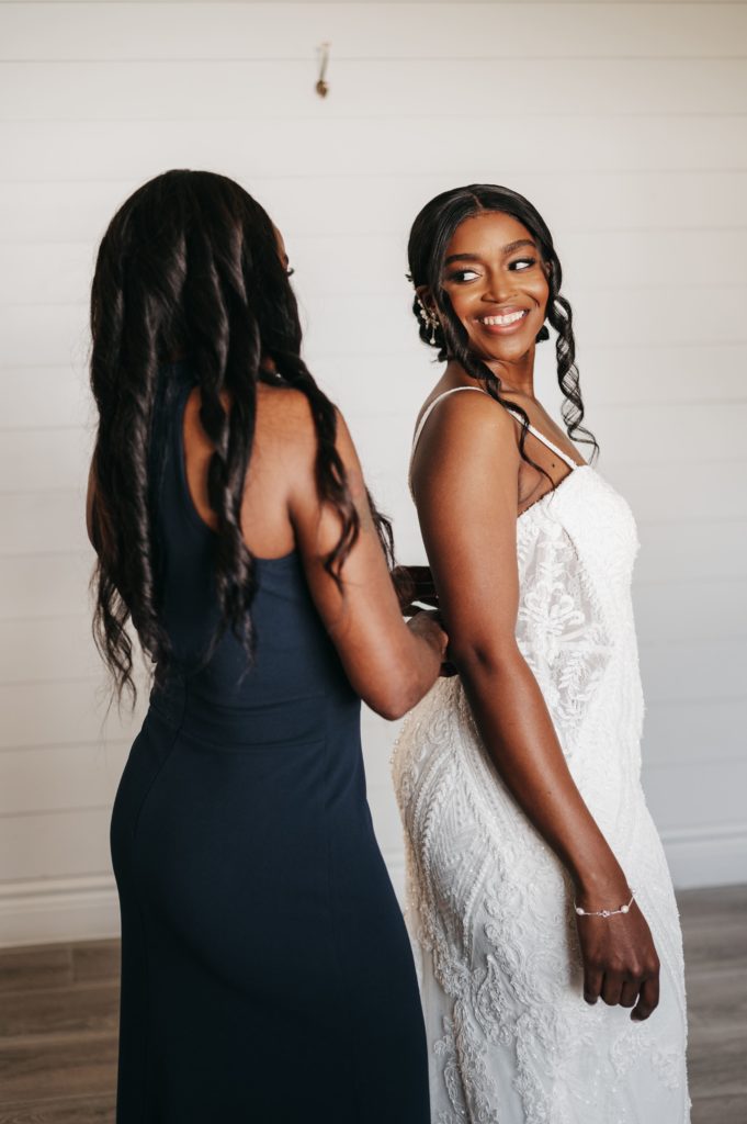 Bride smiles while her dress is getting zipped up for her
