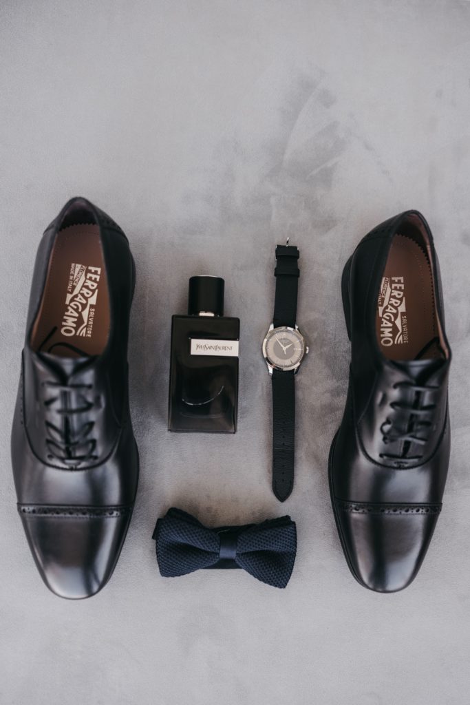 Groom flatlay featuring shoes, a watch, cologne and a bowtie